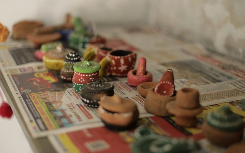 Small, hand-painted clay pots and vessels—showcasing the creativity of local crafts—sit atop colorful newspapers, arranged in rows. Each unique pot features vibrant colors and patterns, capturing the spirit of Gatlinburg Arts & Crafts handmade shops.