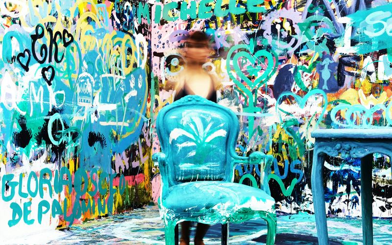 A person with a blurred face stands behind a painted blue chair and table, surrounded by a vibrant, graffiti-covered wall—just the kind of quirky scene you might find among unique Gatlinburg attractions like Ripley’s Believe It or Not Gatlinburg.