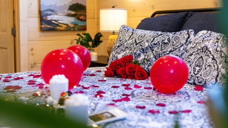 A bed with red balloons, roses and rose petals.