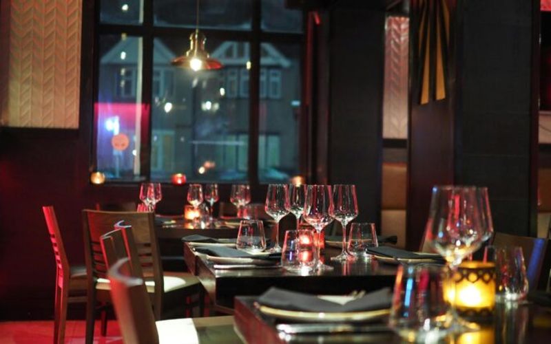 A dimly lit restaurant with tables set with wine glasses, napkins, and candles. The cozy, inviting atmosphere makes it one of the best restaurants Gatlinburg has to offer, with large windows framing views of buildings outside.