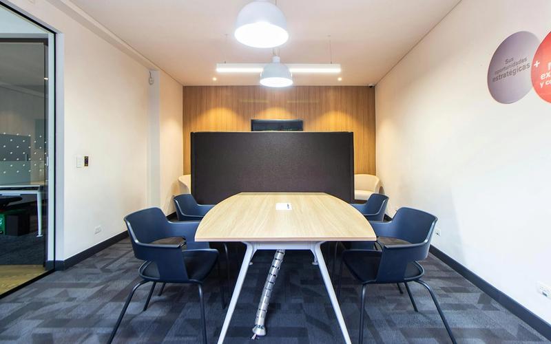 Modern meeting room perfect for corporate retreats or group events, featuring a wooden table, six black chairs, a black partition, white walls with wood paneling, gray carpet, and two ceiling lights. Ideal Meeting Spaces Gatlinburg location.