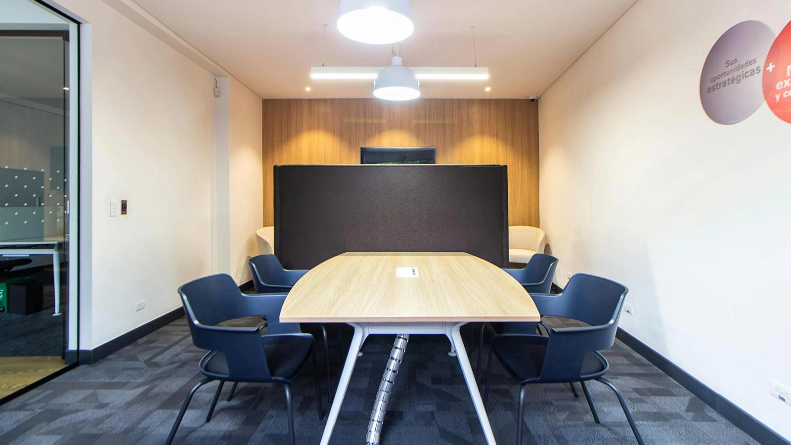 Modern meeting room perfect for corporate retreats or group events, featuring a wooden table, six black chairs, a black partition, white walls with wood paneling, gray carpet, and two ceiling lights. Ideal Meeting Spaces Gatlinburg location.