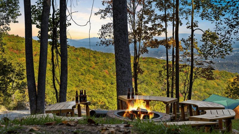 View of wooden benches in the forest around a campfire. Stunning views of the forest and valley in the background.