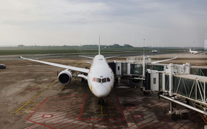 A white commercial airplane is parked at an airport gate, connected to passenger bridges, with an empty tarmac and overcast sky—typical of the closest airports to Gatlinburg for convenient Gatlinburg travel.