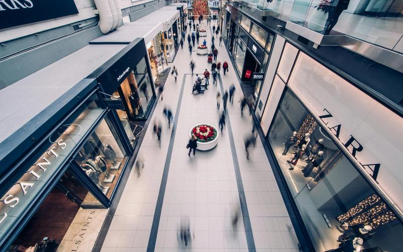 Aerial view of the busy Tanger Outlets Sevierville with blurred shoppers walking between store displays and clothing brand storefronts under bright lighting, perfect for vibrant shopping photos.