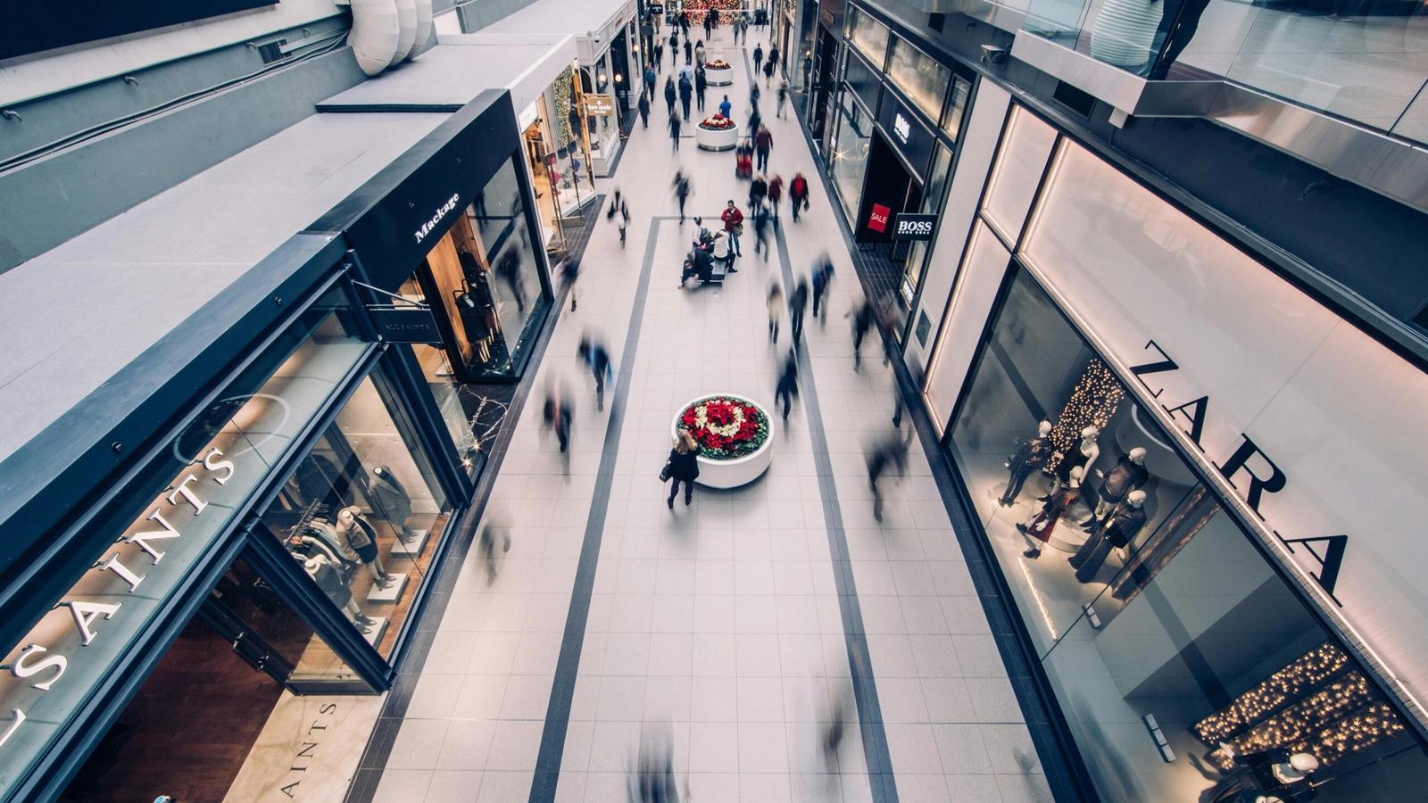 Aerial view of the busy Tanger Outlets Sevierville with blurred shoppers walking between store displays and clothing brand storefronts under bright lighting, perfect for vibrant shopping photos.