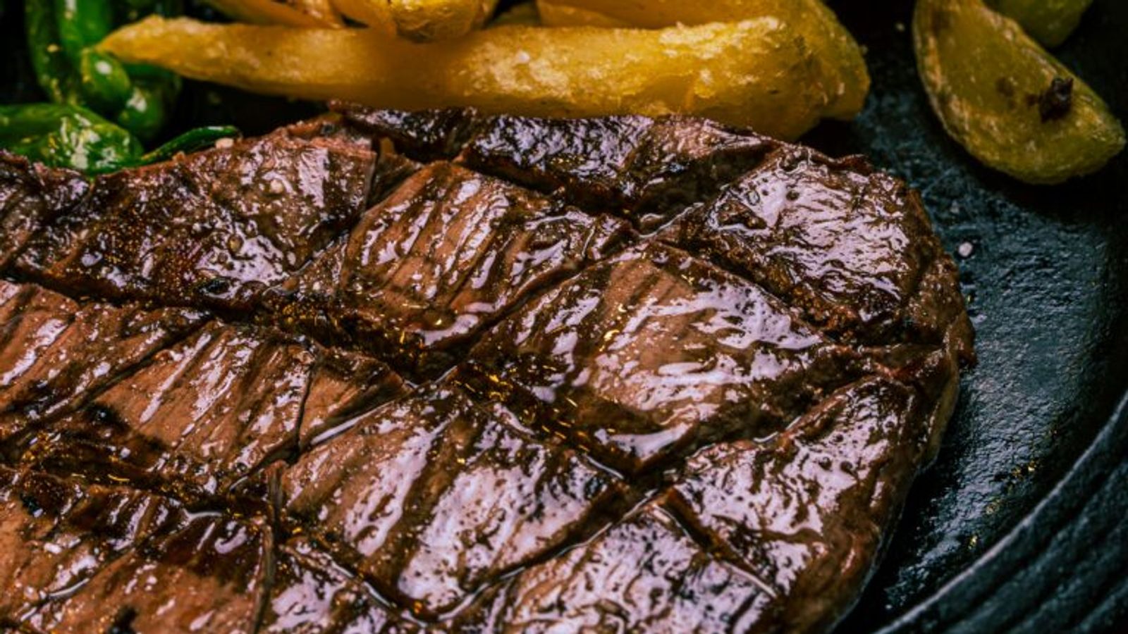 Close-up of a grilled steak with grill marks, served with golden French fries and green vegetables on a dark plate—just like you'd find on the Peddler Steakhouse menu. The steak appears juicy and cooked to perfection.