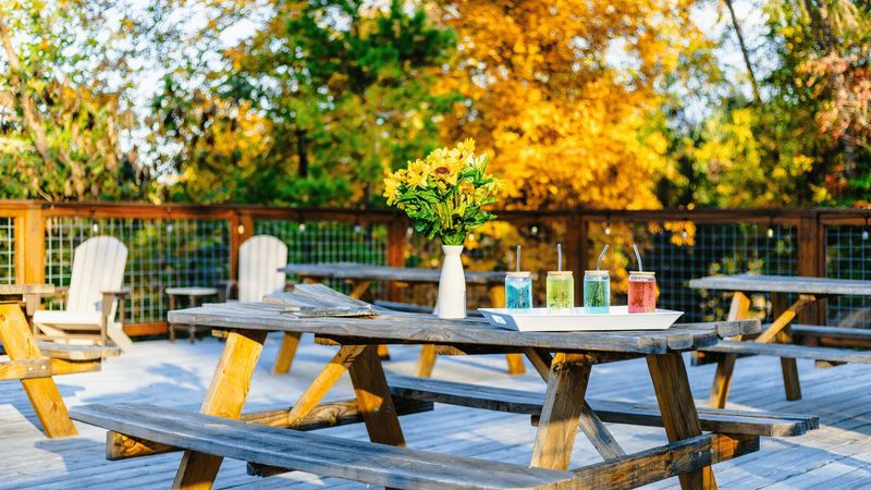 An outdoor bench with drinks and flowers. Chairs and benches can be seen in the background.