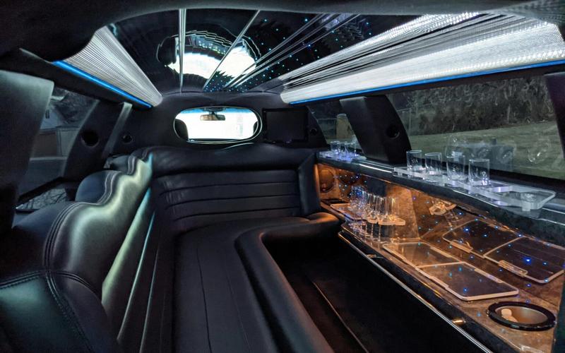Interior of a luxury limousine featuring black leather seats, a mirrored ceiling with blue lights, and a bar area with glasses and cupholders—perfect for shuttle services around Pigeon Forge or exploring the scenic Smoky Mountains in style.