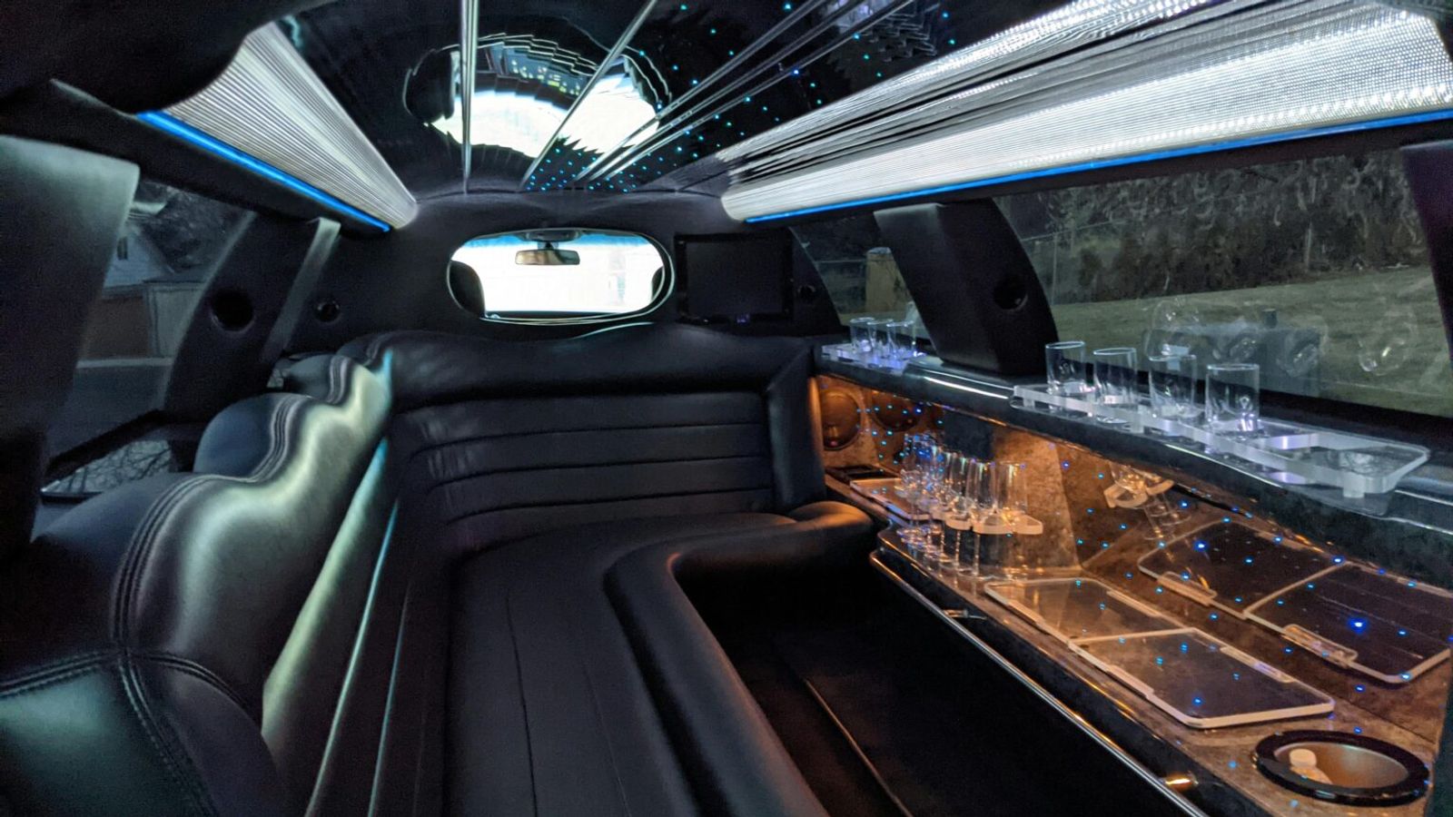 Interior of a luxury limousine featuring black leather seats, a mirrored ceiling with blue lights, and a bar area with glasses and cupholders—perfect for shuttle services around Pigeon Forge or exploring the scenic Smoky Mountains in style.