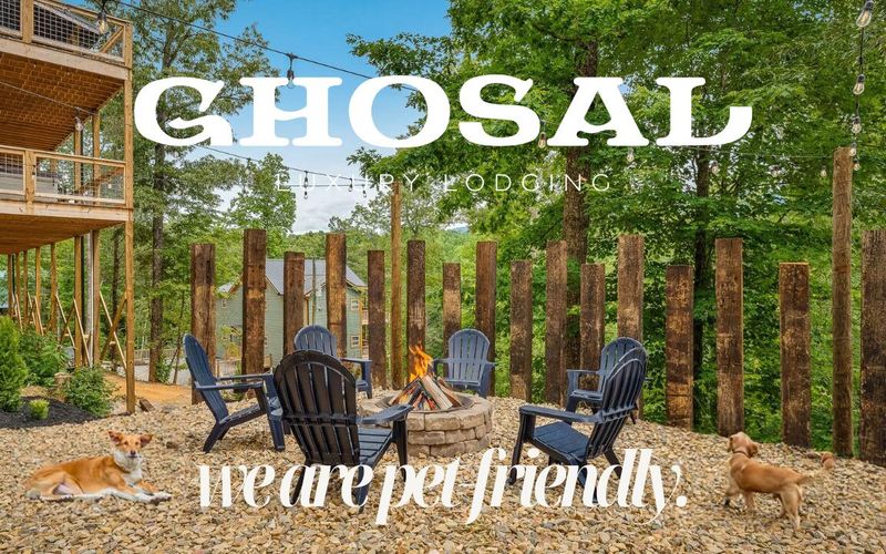 Outdoor fire pit area with Adirondack chairs, surrounded by tall wooden posts and trees in Gatlinburg. Two dogs are nearby. Text reads, “GHOSAL Luxury Lodging. We are pet friendly—enjoy Pet-Friendly Activities.”.