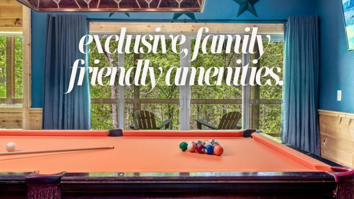 A bright game room with an orange pool table, cue stick, and billiard balls. Large windows overlook a deck with Adirondack chairs and green trees. Why We Stand Out: exclusive, family-friendly amenities.