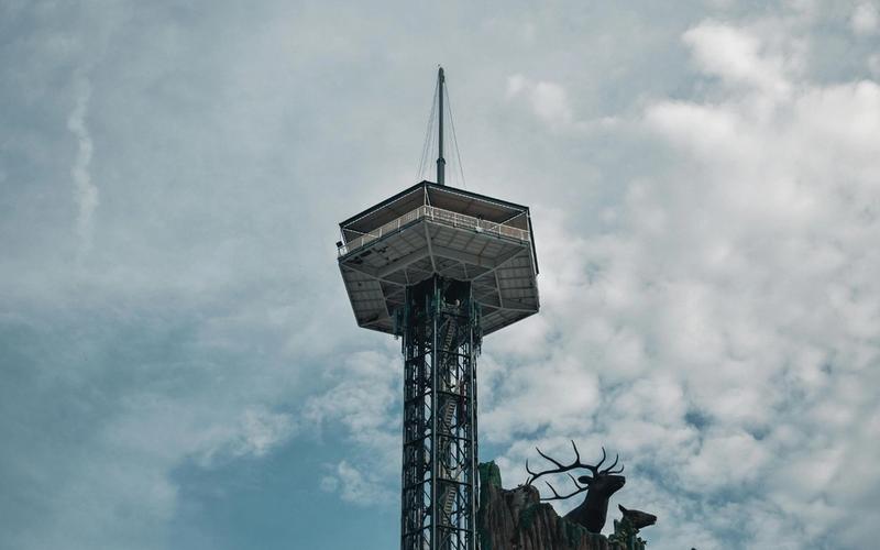 A tall observation tower with a pointed spire, the Gatlinburg Space Needle, rises against a cloudy sky; below, silhouettes of a large stag and small deer stand near the edge of a rocky structure—a classic scene among things to do in Gatlinburg.