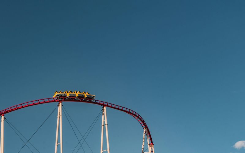 A thrilling roller coaster at Dollywood rides to the peak of a steep red track, its yellow cars poised against a clear blue sky and supported by sturdy white beams.