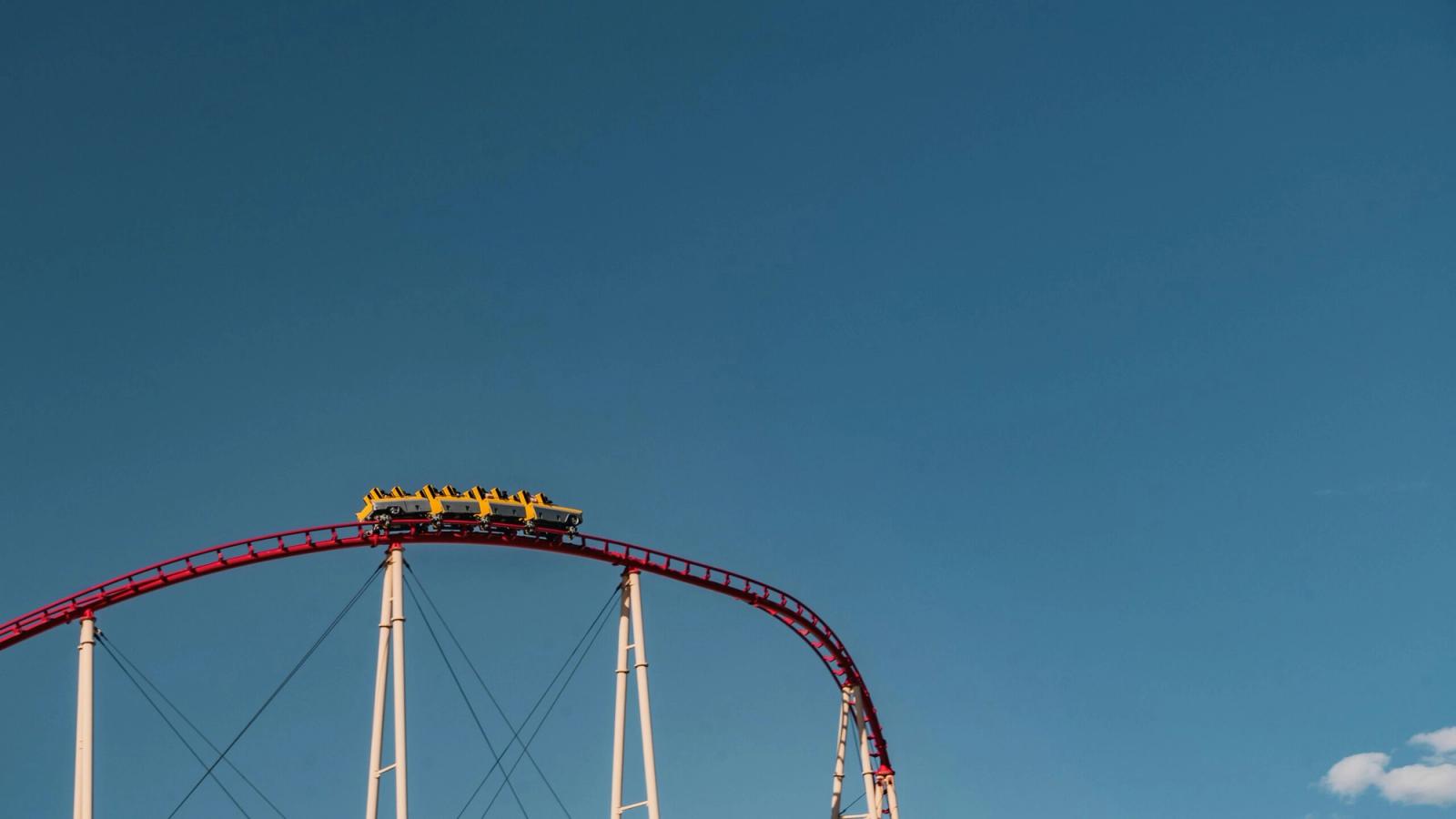 A thrilling roller coaster at Dollywood rides to the peak of a steep red track, its yellow cars poised against a clear blue sky and supported by sturdy white beams.