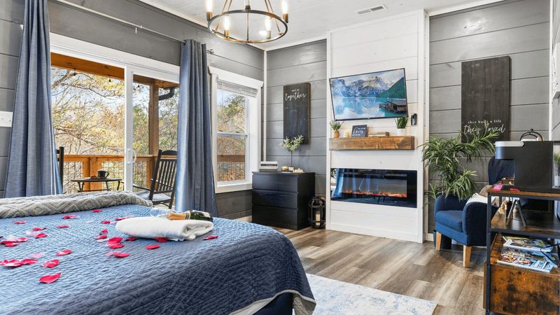 A bedroom area. A bottle of champagne rests on a towel on the bed. There is a wall mounted tv and fire.