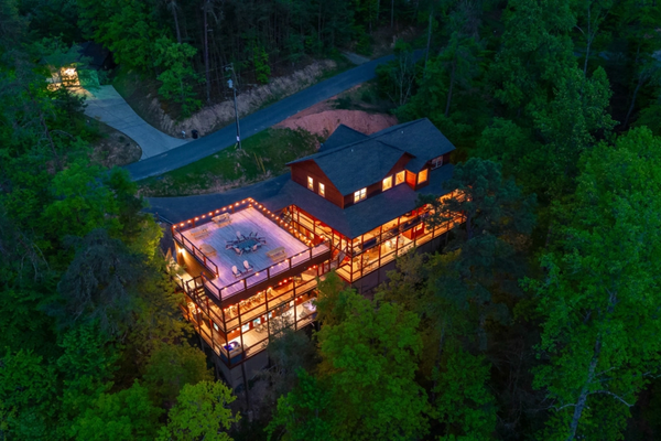 Large group cabin lit with string lights in a forested mountain setting.