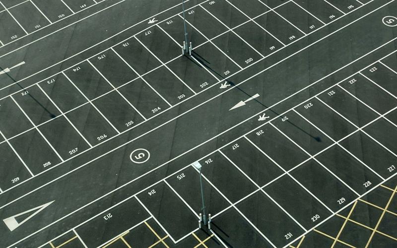 Aerial view of an empty, freshly painted parking lot with white-lined spaces, numbers on each space, arrows indicating directions, and several light poles casting long shadows—ideal for anyone seeking free parking near Gatlinburg parking garages.
