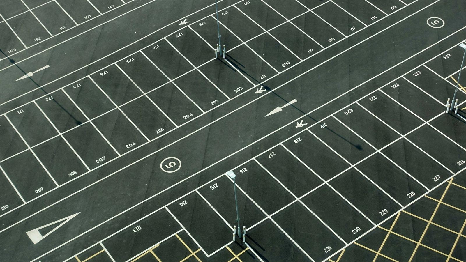 Aerial view of an empty, freshly painted parking lot with white-lined spaces, numbers on each space, arrows indicating directions, and several light poles casting long shadows—ideal for anyone seeking free parking near Gatlinburg parking garages.