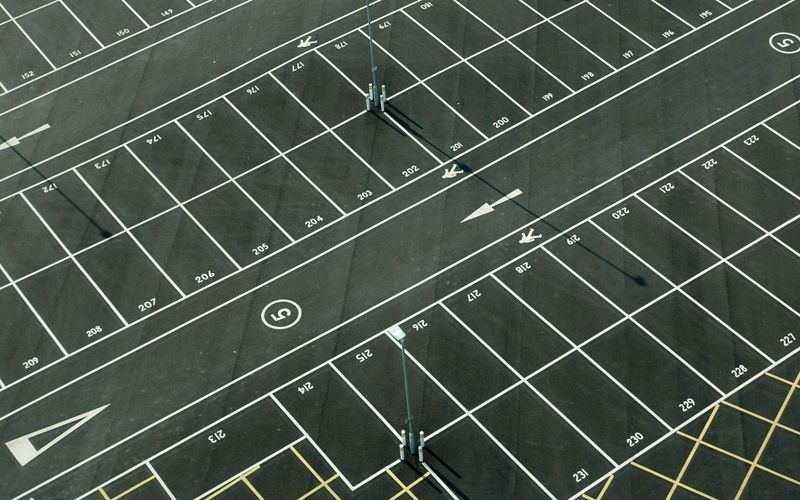 Aerial view of an empty, freshly painted parking lot with white-lined spaces, numbers on each space, arrows indicating directions, and several light poles casting long shadows—ideal for anyone seeking free parking near Gatlinburg parking garages.