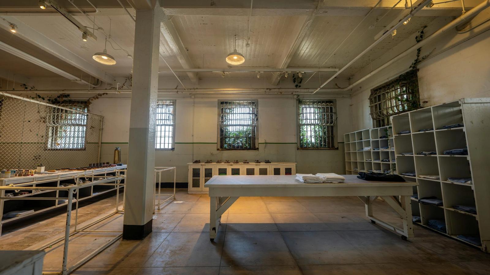Large, empty room with barred windows, metal shelving, and tables with folded linens—like a prison laundry at Alcatraz East Crime Museum in Pigeon Forge. Industrial lighting and worn floors complete the scene. Tickets available for tours.