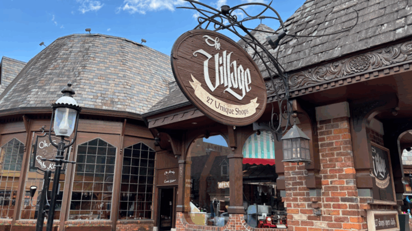 A rustic brick and wood building with a sign reading “The Village: 27 Unique Shops.” The curved shingle roofs and large windows evoke old-world charm, making the Village Shops Gatlinburg a must-see for memorable Gatlinburg shopping.
