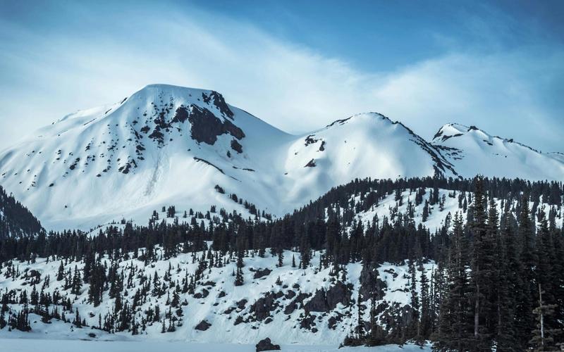 Snow-covered mountain peaks rise under a blue sky, with dark pine trees covering the lower slopes and patches of exposed rock—one of the many stunning sights to enjoy among the things to do in Gatlinburg in winter.