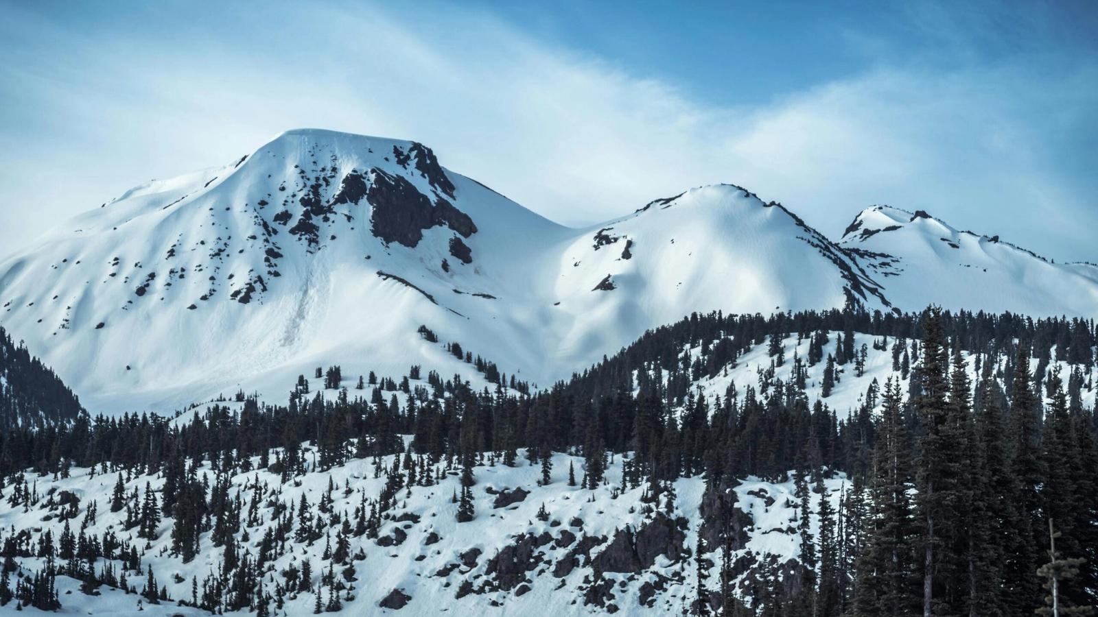 Snow-covered mountain peaks rise under a blue sky, with dark pine trees covering the lower slopes and patches of exposed rock—one of the many stunning sights to enjoy among the things to do in Gatlinburg in winter.