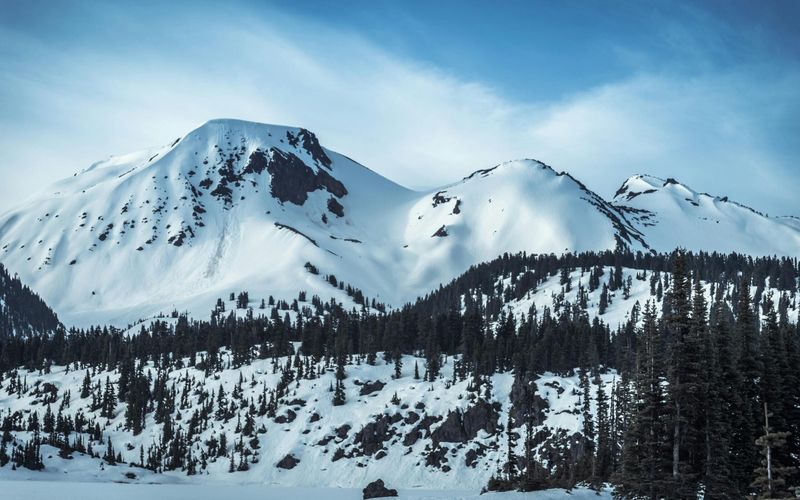 Snow-covered mountain peaks rise under a blue sky, with dark pine trees covering the lower slopes and patches of exposed rock—one of the many stunning sights to enjoy among the things to do in Gatlinburg in winter.