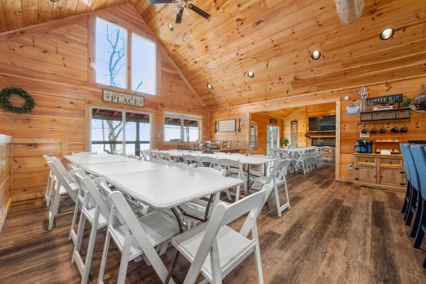 Bright, spacious, and ready for gatherings or events, this large wooden room with a vaulted ceiling features several long white folding tables and chairs, large windows, a coffee station, and rustic décor—embodying the inviting charm found in Smoky Mountain Cabins.