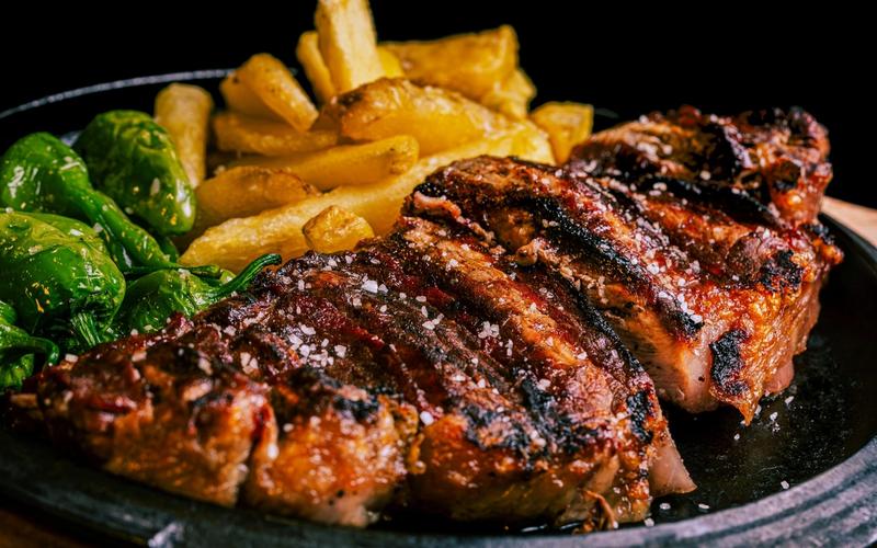 Grilled steak sliced and sprinkled with coarse salt, served with golden fries and green peppers—just like a signature dish at Greenbrier Restaurant in Gatlinburg—presented on a black plate against a dark background.