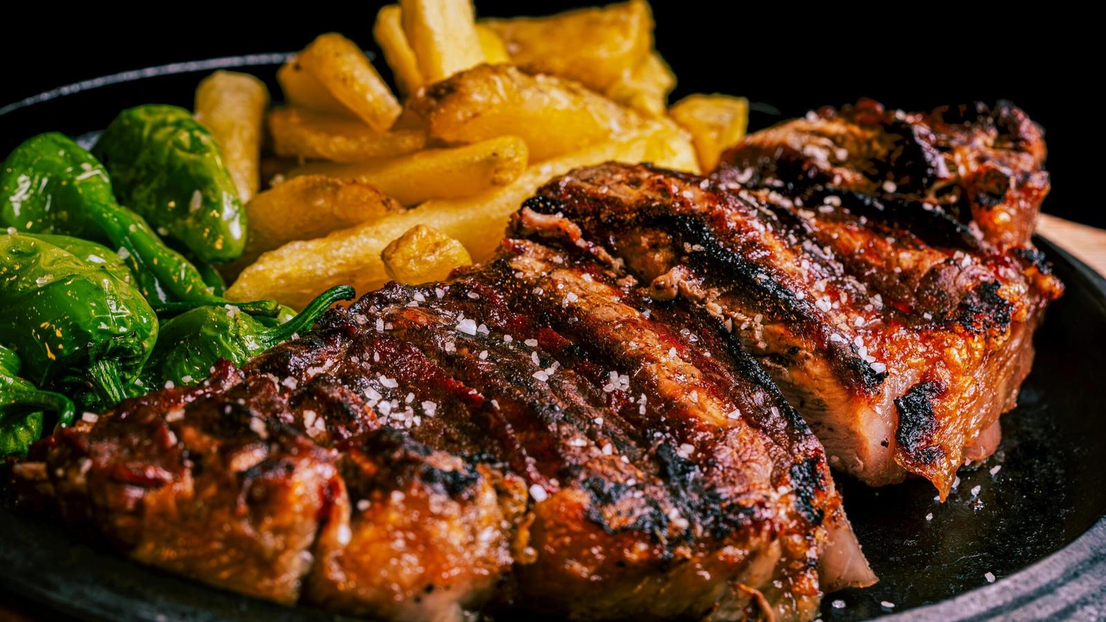 Grilled steak sliced and sprinkled with coarse salt, served with golden fries and green peppers—just like a signature dish at Greenbrier Restaurant in Gatlinburg—presented on a black plate against a dark background.