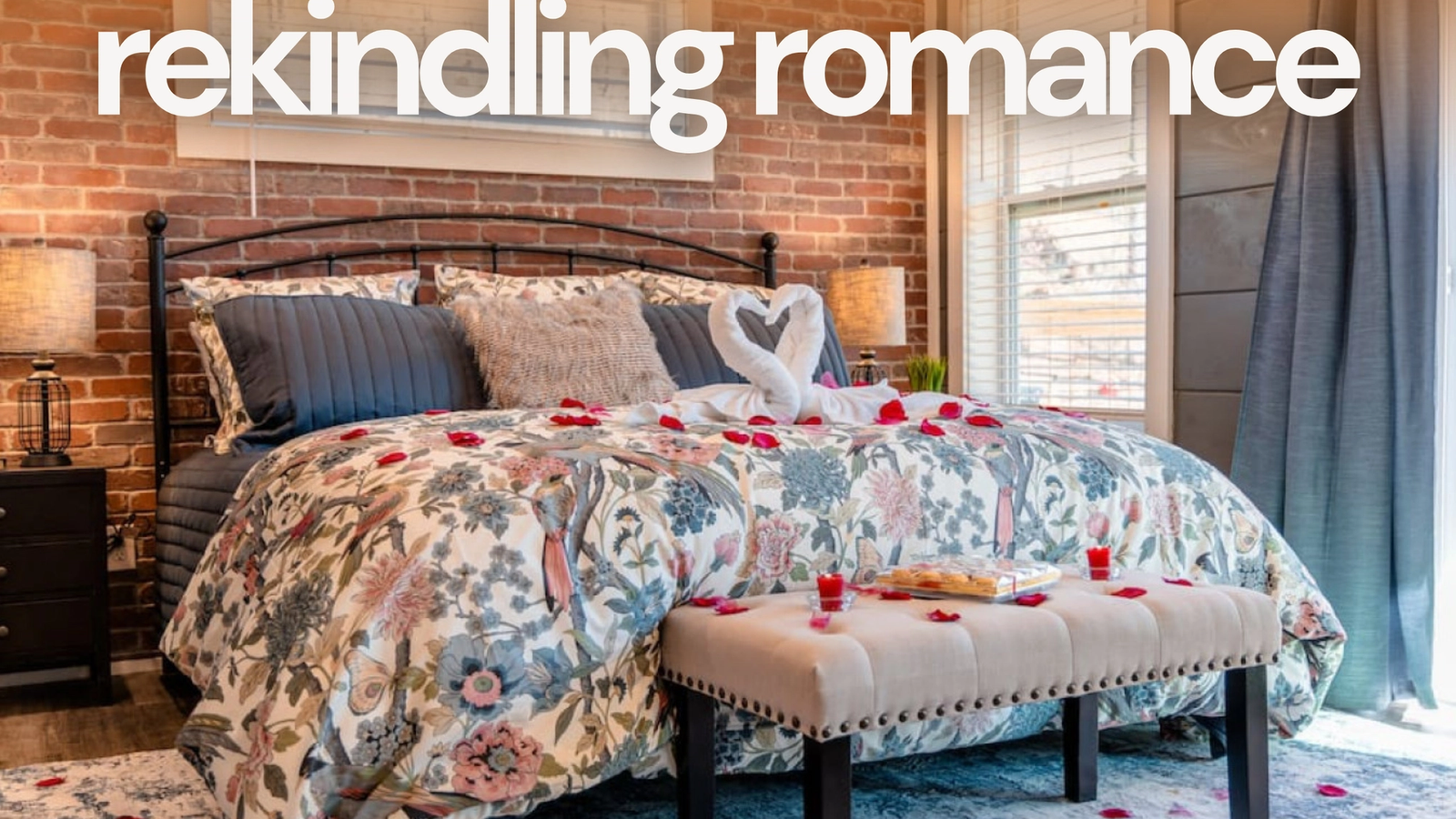 A cozy bedroom with a floral bedspread, swan towels, and rose petals on the bed sets the scene for a couples retreat. Warm lighting and brick walls create a romantic atmosphere, with "rekindling romance" in large white text above.