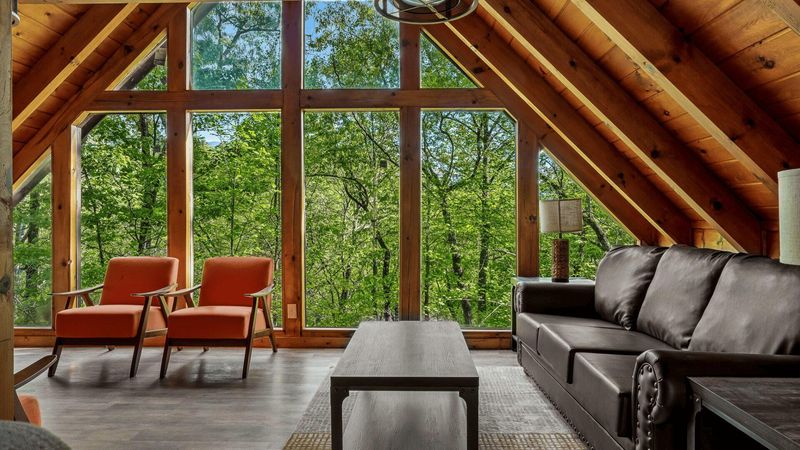 A living area with a sofa and two chairs, with large windows in the background.