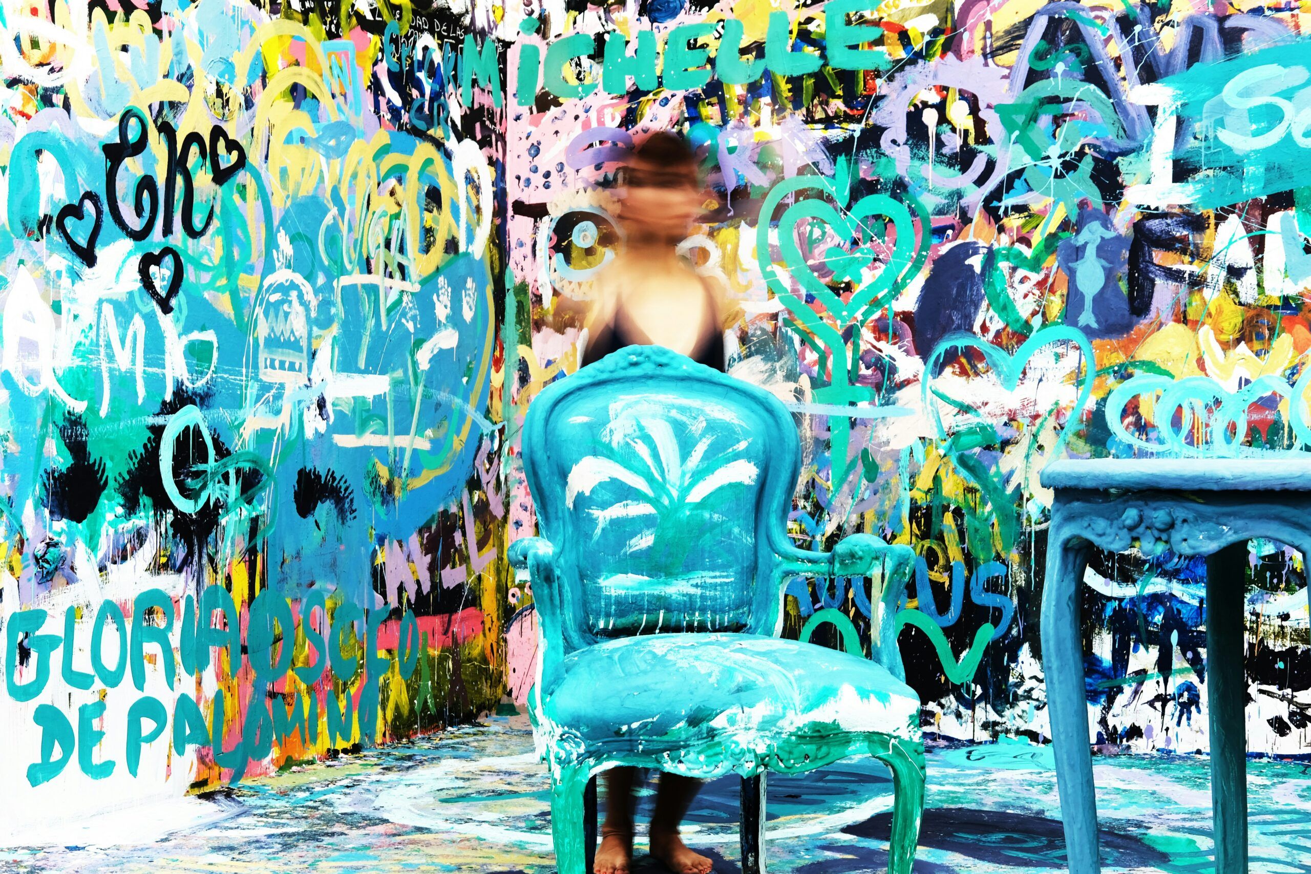 A person with a blurred face stands behind a painted blue chair and table, surrounded by a vibrant, graffiti-covered wall—just the kind of quirky scene you might find among unique Gatlinburg attractions like Ripley’s Believe It or Not Gatlinburg.