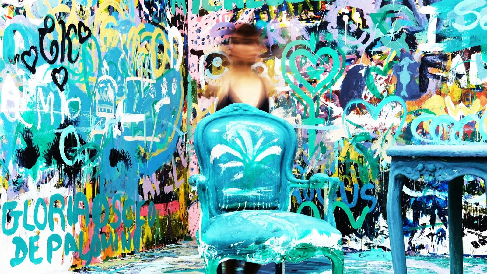 A person with a blurred face stands behind a painted blue chair and table, surrounded by a vibrant, graffiti-covered wall—just the kind of quirky scene you might find among unique Gatlinburg attractions like Ripley’s Believe It or Not Gatlinburg.