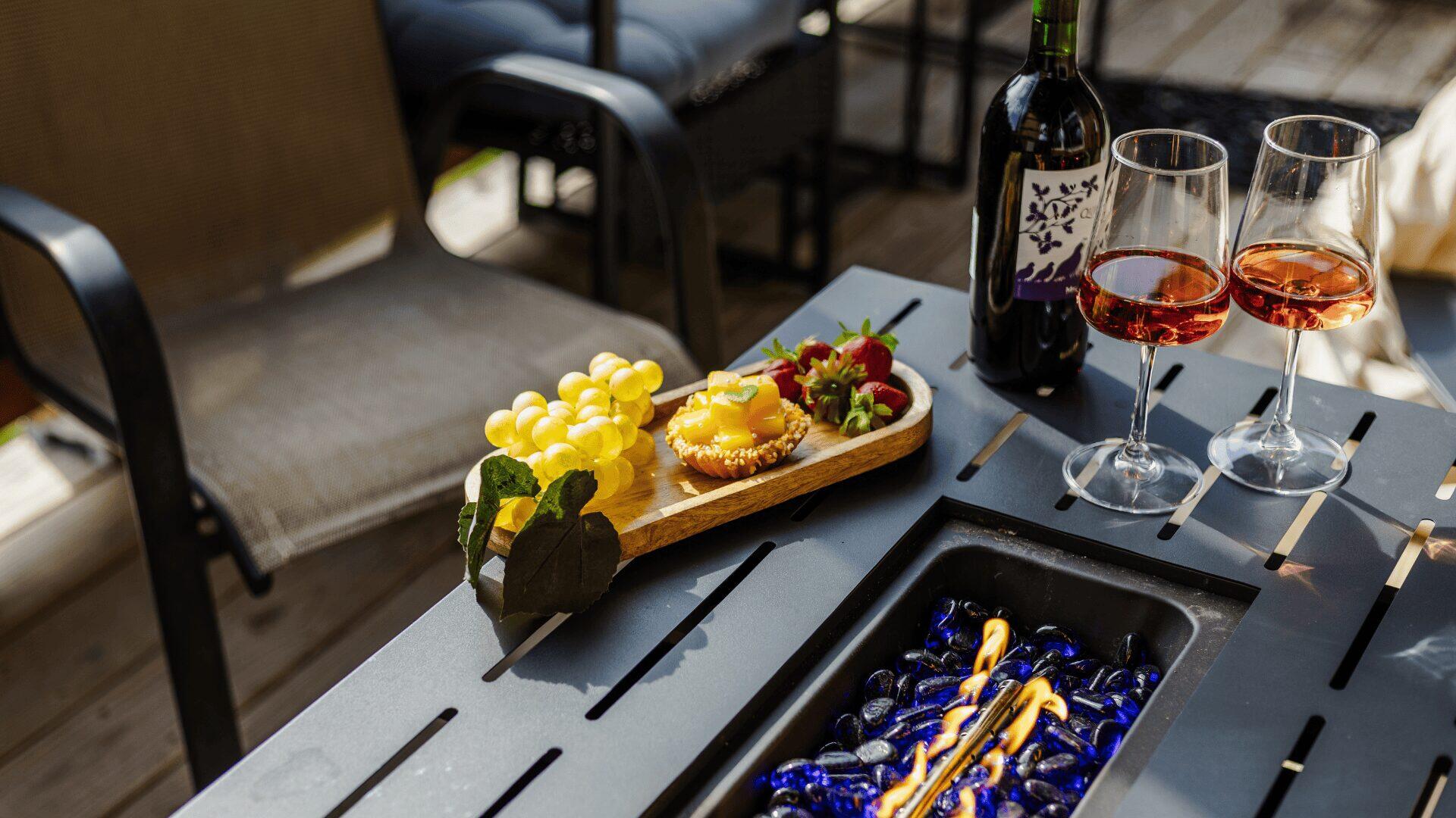 A bottle of wine with two glasses along with a selection of fruit snacks on a table.