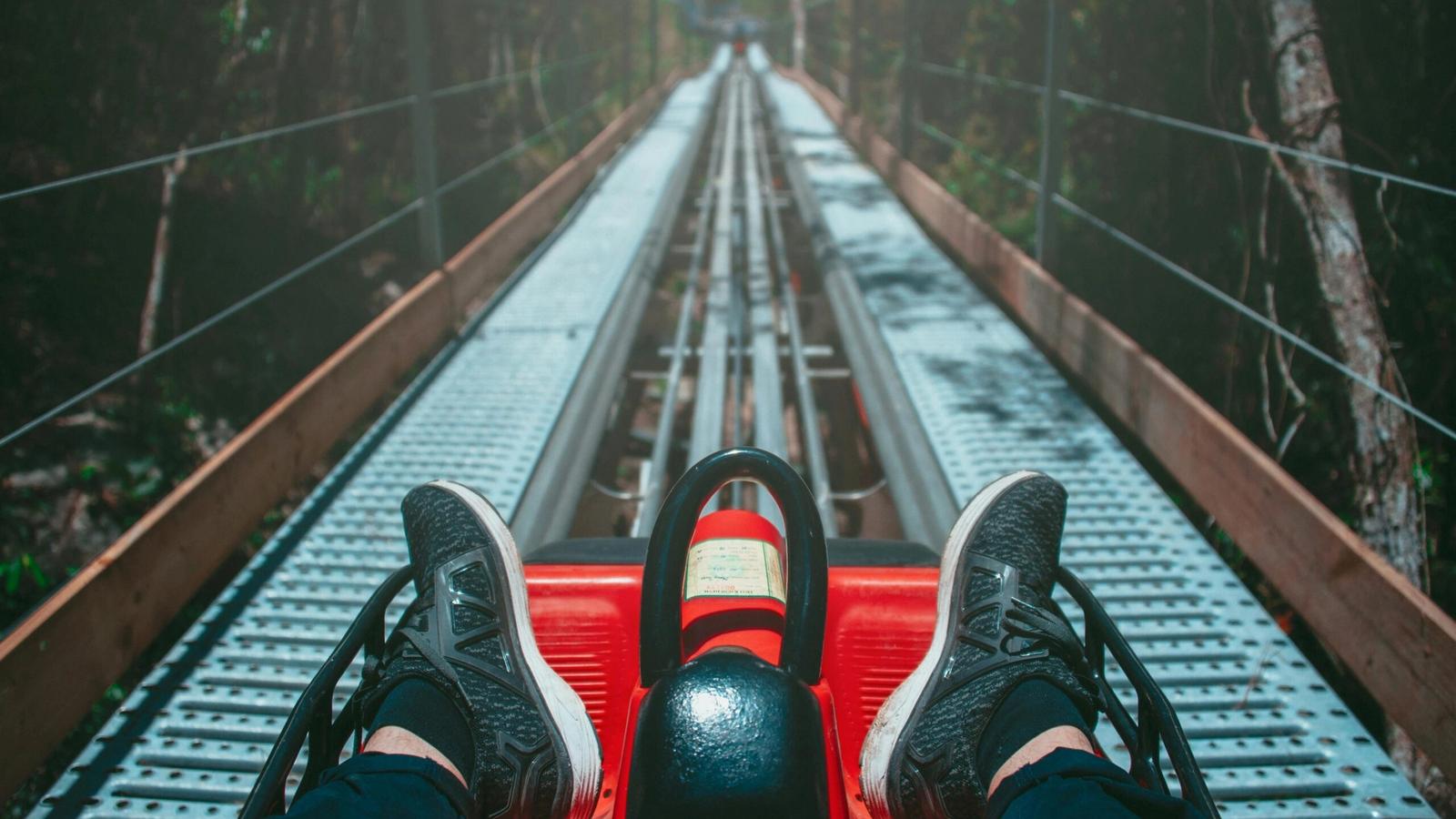 Riding a red alpine coaster down a metal track in the forest, with black sneakers visible and the track stretching ahead—experience one of the best mountain coasters in the Smoky Mountains.