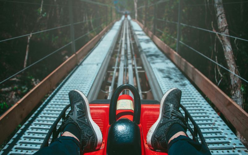 Riding a red alpine coaster down a metal track in the forest, with black sneakers visible and the track stretching ahead—experience one of the best mountain coasters in the Smoky Mountains.