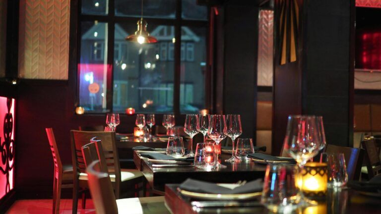 A dimly lit restaurant with tables set with wine glasses, napkins, and candles. The cozy, inviting atmosphere makes it one of the best restaurants Gatlinburg has to offer, with large windows framing views of buildings outside.