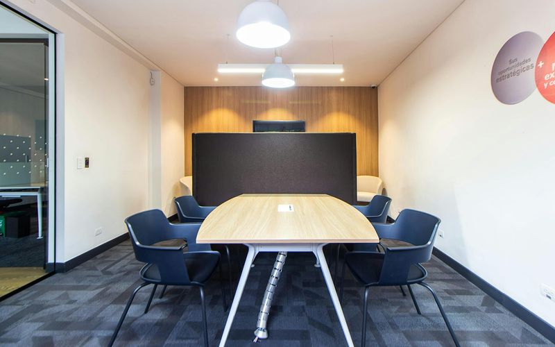Modern meeting room perfect for corporate retreats or group events, featuring a wooden table, six black chairs, a black partition, white walls with wood paneling, gray carpet, and two ceiling lights. Ideal Meeting Spaces Gatlinburg location.
