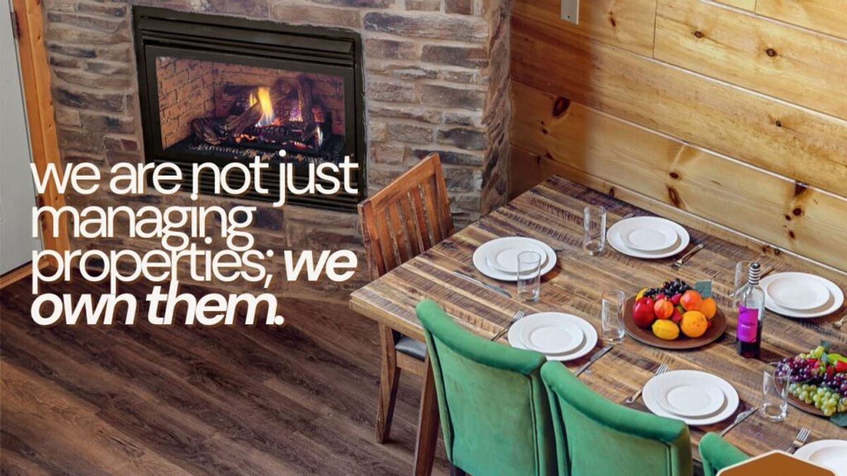 A cozy dining area with a wooden table set for six, green chairs, a bowl of fruit, and a fireplace with a lit fire. Text reads: we stand out because we are not just managing properties; we own them.