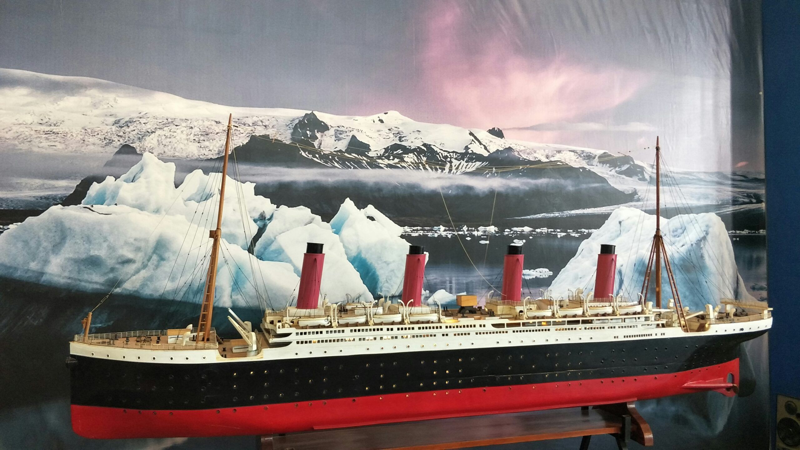 A large model of the Titanic ship is displayed at this popular Pigeon Forge attraction, set against a backdrop of icy waters, icebergs, and snow-covered mountains beneath a pink and purple sky—perfect for fans of the Titanic Museum.