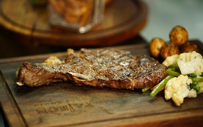 A grilled steak served on a wooden board with a side of mixed vegetables, including green beans, cauliflower, and mushrooms—just one highlight from the Cherokee Grill menu in Gatlinburg TN.