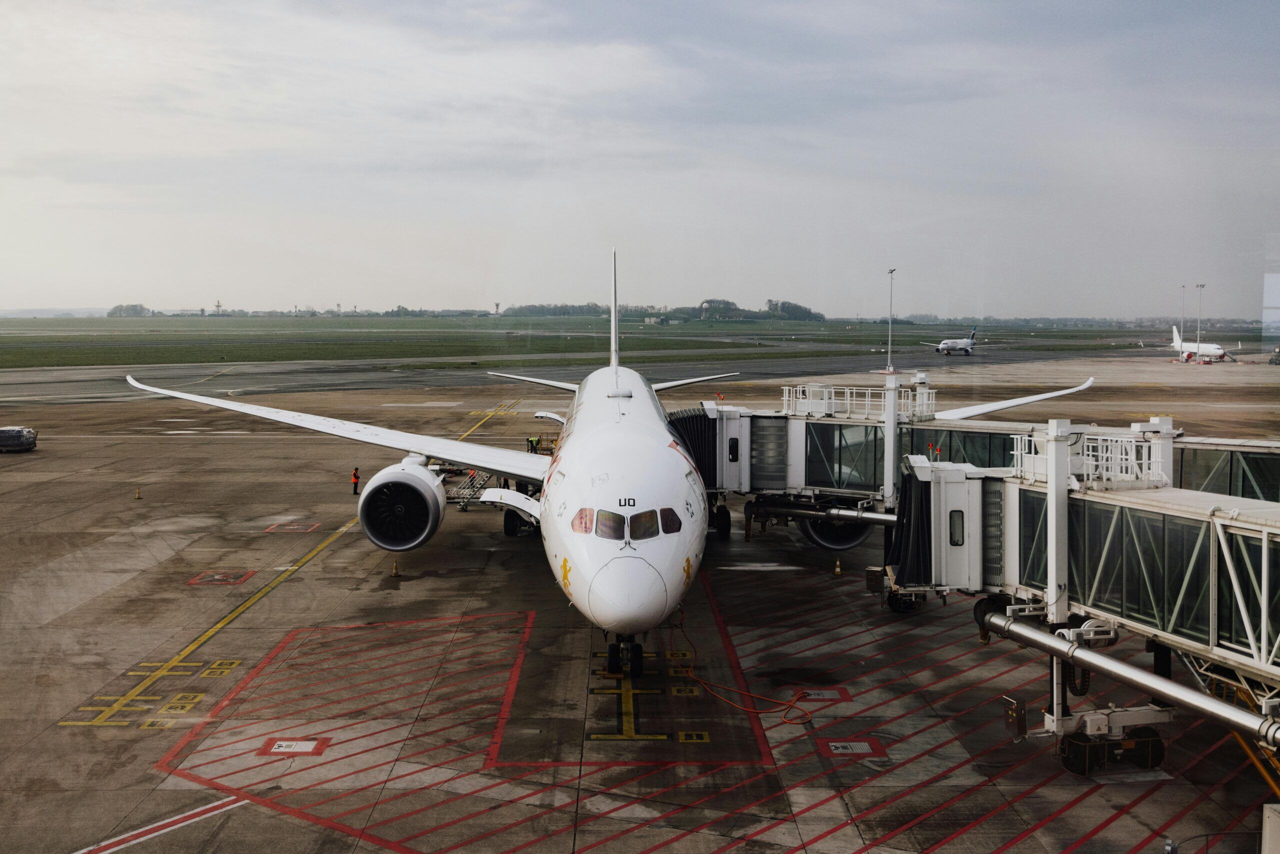 A white commercial airplane is parked at an airport gate, connected to passenger bridges, with an empty tarmac and overcast sky—typical of the closest airports to Gatlinburg for convenient Gatlinburg travel.