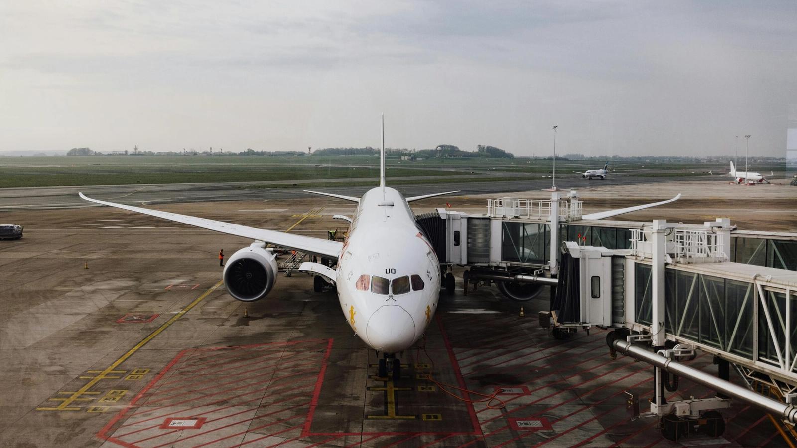 A white commercial airplane is parked at an airport gate, connected to passenger bridges, with an empty tarmac and overcast sky—typical of the closest airports to Gatlinburg for convenient Gatlinburg travel.