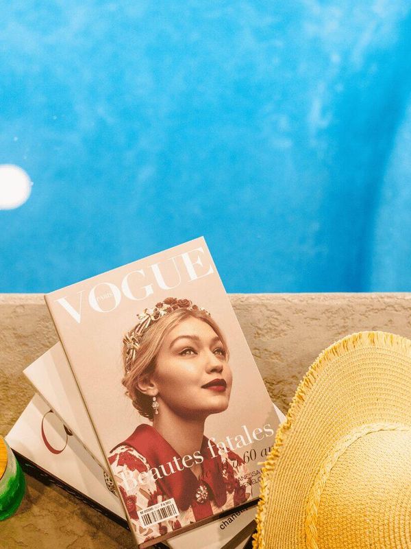 A Vogue magazine next to a pool, with a sun hat and two drinks.
