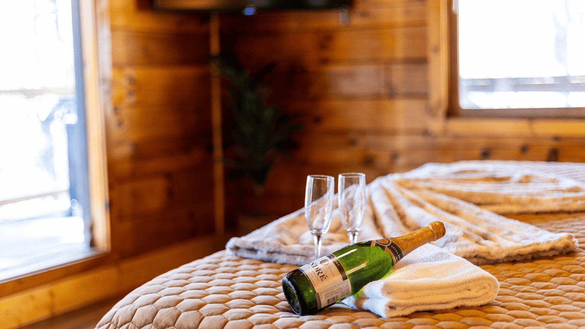 A bottle of champagne resting on a towel with two glasses beside it.