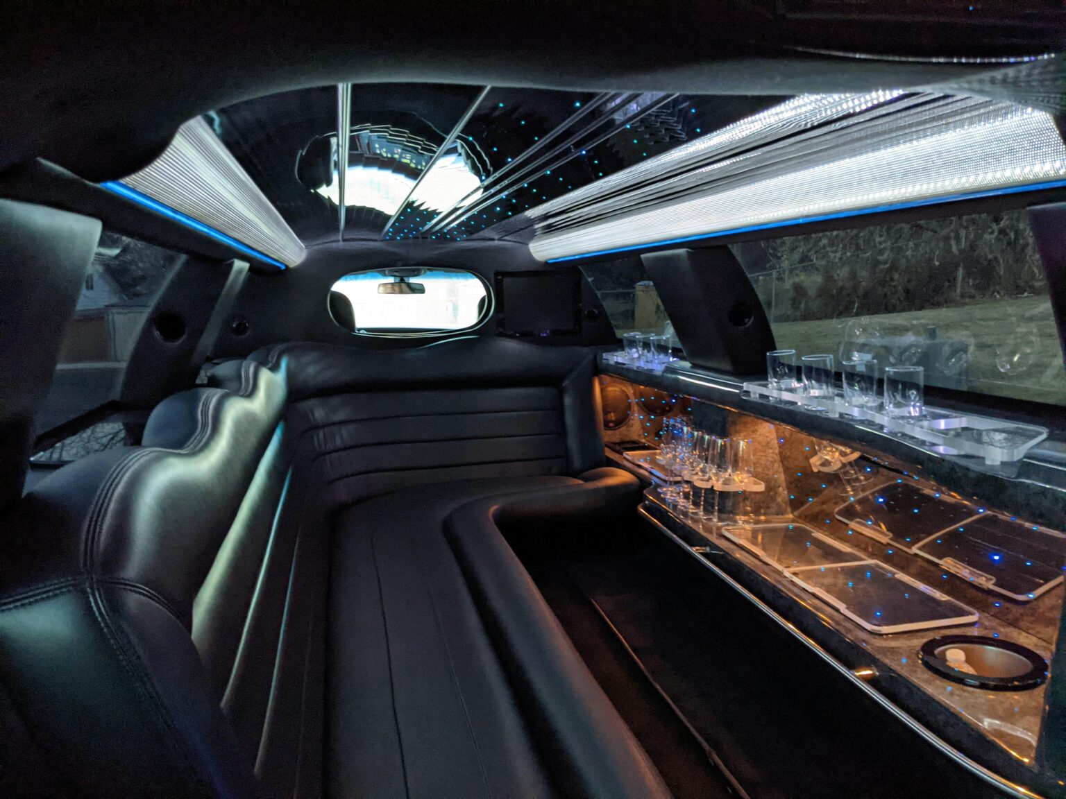 Interior of a luxury limousine featuring black leather seats, a mirrored ceiling with blue lights, and a bar area with glasses and cupholders—perfect for shuttle services around Pigeon Forge or exploring the scenic Smoky Mountains in style.