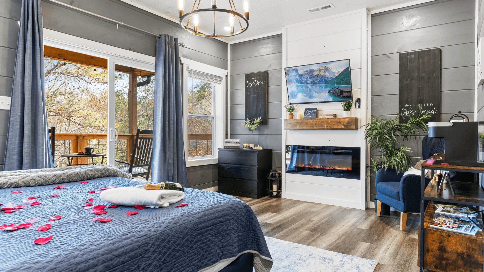 A bedroom area. A bottle of champagne rests on a towel on the bed. There is a wall mounted tv and fire.